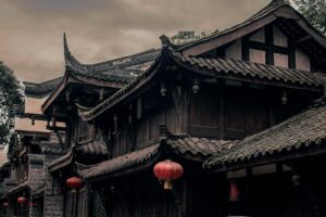 Historic Chinese building with ornate roofs and red lanterns under cloudy skies.