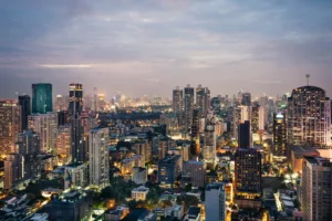 A dense cityscape of Bangkok at twilight with illuminated skyscrapers and office buildings